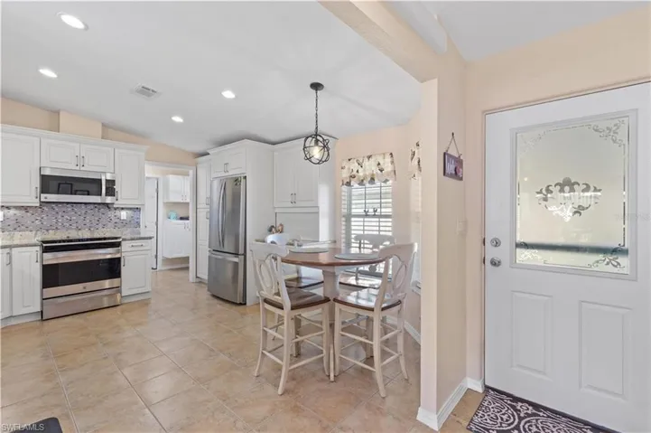 Kitchen with stainless steel appliances, white cabinetry, backsplash, light stone countertops, and hanging light fixtures