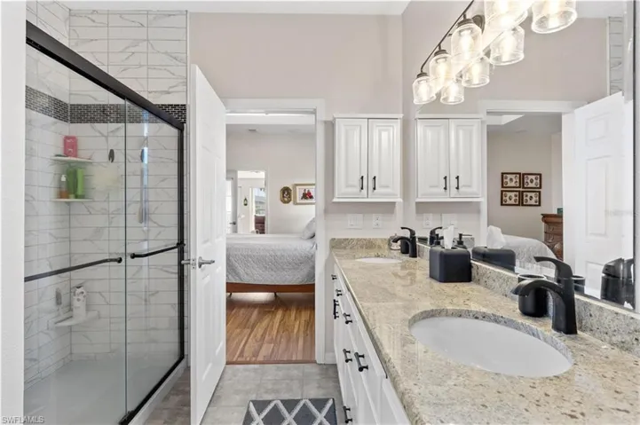 Bathroom with connected bathroom, double vanity, a stall shower, and light tile patterned flooring