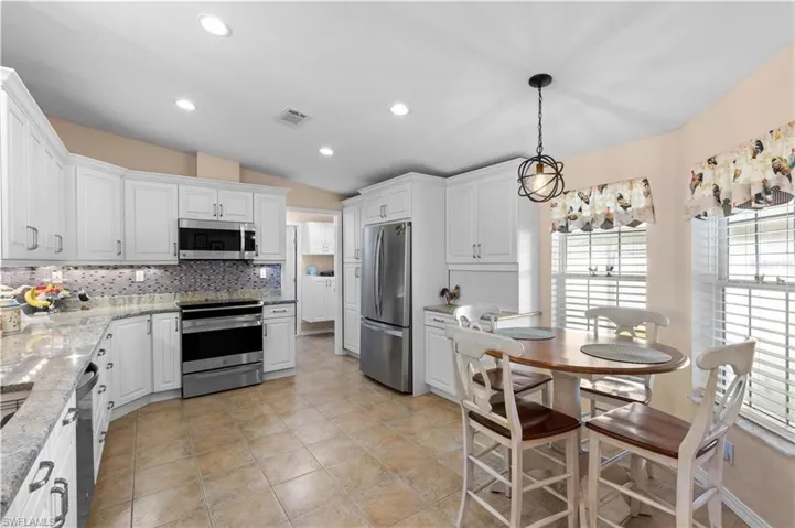 Kitchen with lofted ceiling, stainless steel appliances, white cabinets, light stone countertops, and tasteful backsplash