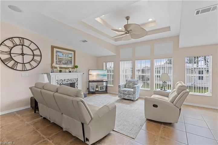 Living area with a fireplace, ceiling fan, a tray ceiling, light tile patterned floors, and recessed lighting