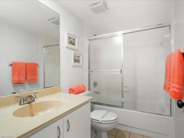 Full bath featuring tile patterned flooring, toilet, vanity, and enclosed tub / shower combo
