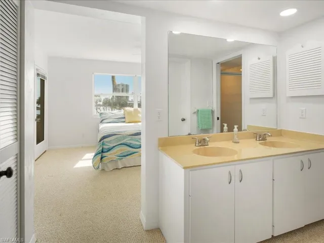 Ensuite bathroom featuring double vanity, baseboards, recessed lighting, and a closet