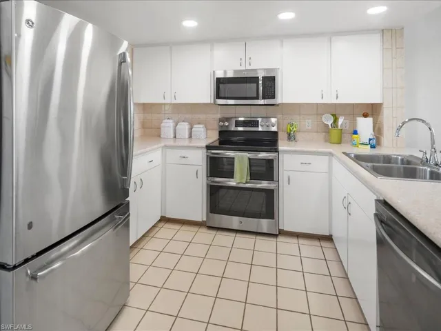 Kitchen with stainless steel appliances, a sink, decorative backsplash, light countertops, and recessed lighting