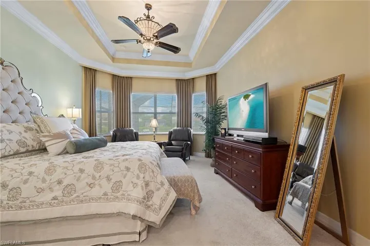 Carpeted primary bedroom featuring crown molding, ceiling fan, and a raised ceiling