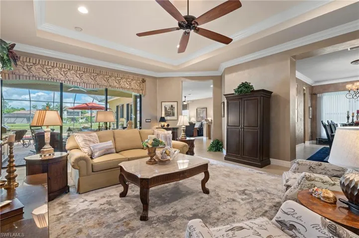 Tiled living room with crown molding, a raised ceiling, and ceiling fan with notable chandelier