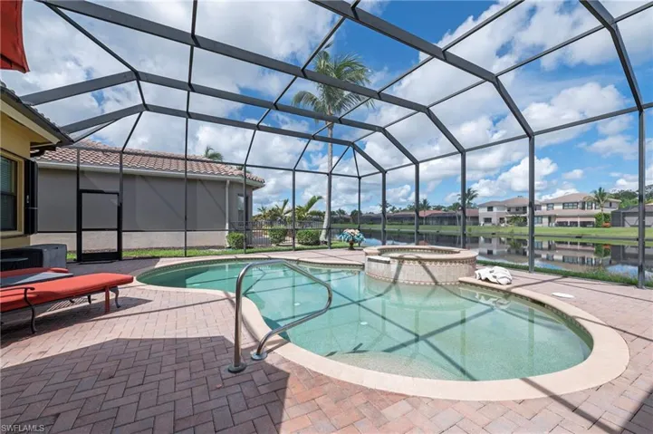 View of pool featuring a patio area, a water view, glass enclosure, and an in ground hot tub
