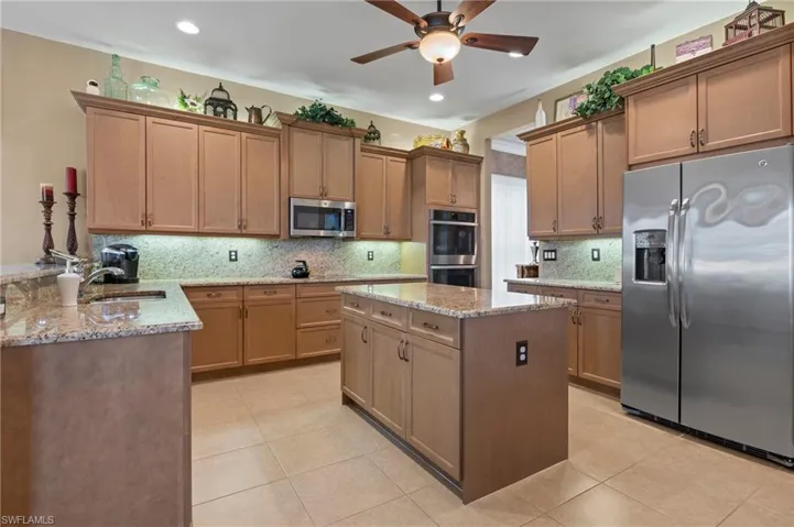 Kitchen featuring ceiling fan, light stone counters, tasteful backsplash, and appliances with stainless steel finishes