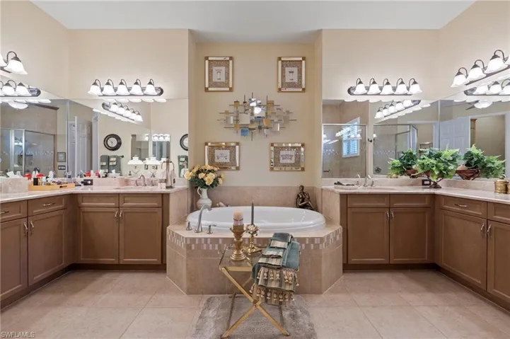 Primary Bathroom featuring tile floors, a relaxing tiled bath, double sink, and vanity with extensive cabinet space
