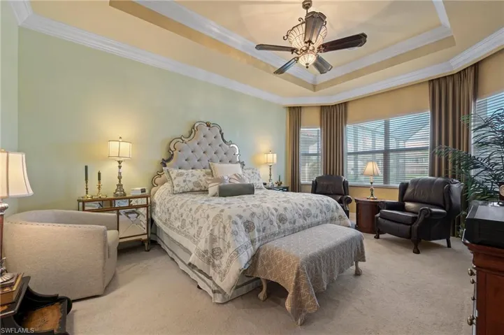 Primary bedroom with crown molding, carpet floors, ceiling fan, and a raised ceiling