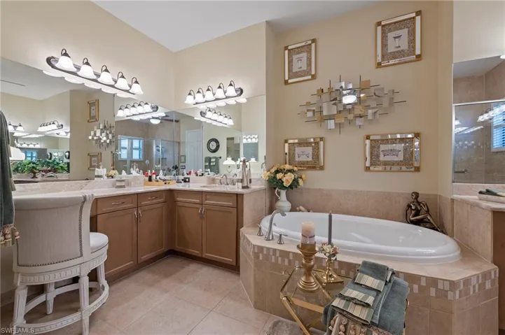 Primary Bathroom featuring a healthy amount of sunlight, vanity with extensive cabinet space, tiled tub, and tile floors