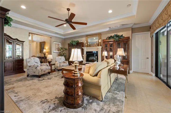 Tiled living room with ceiling fan, a tray ceiling, and crown molding