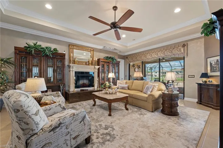 Living room featuring ornamental molding, light tile flooring, ceiling fan, electric fireplace and a raised ceiling