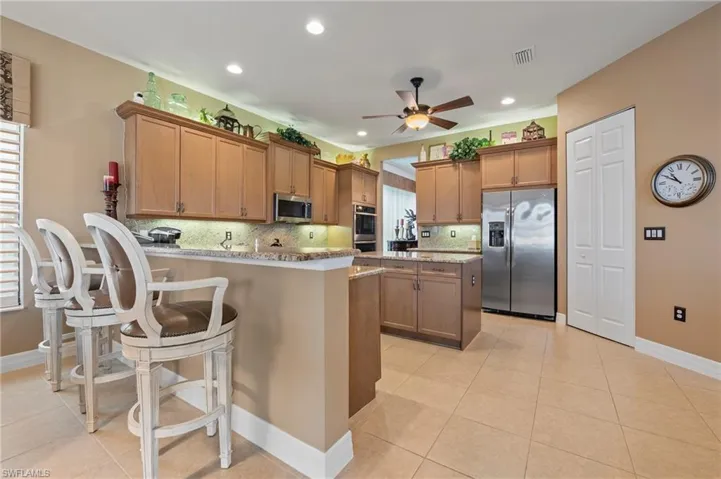 Kitchen featuring stainless steel appliances, light stone counters, tasteful backsplash, ceiling fan, and light tile floors