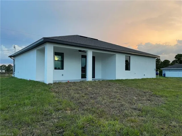 Rear view of property featuring ceiling fan, a lawn, stucco siding, and roof with shingles