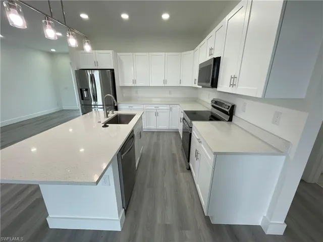 Kitchen featuring wood finished floors, stainless steel appliances, recessed lighting, a center island with sink, and white cabinetry