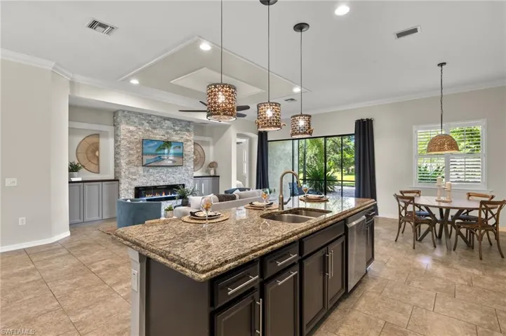 Kitchen with light stone counters, a stone fireplace, ceiling fan, a center island with sink, and sink