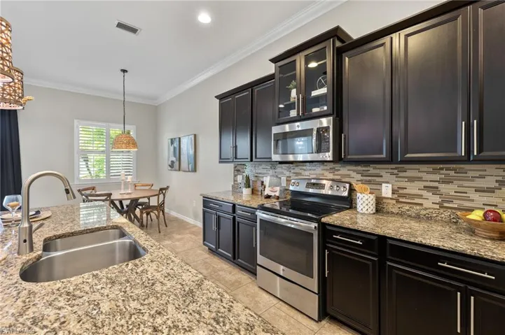 Kitchen with backsplash, pendant lighting, stainless steel appliances, ornamental molding, and sink