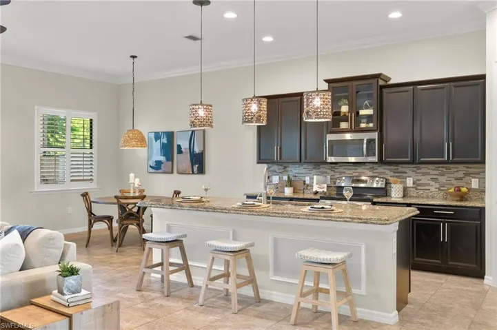 Kitchen with pendant lighting, stainless steel appliances, light stone counters, and a center island with sink
