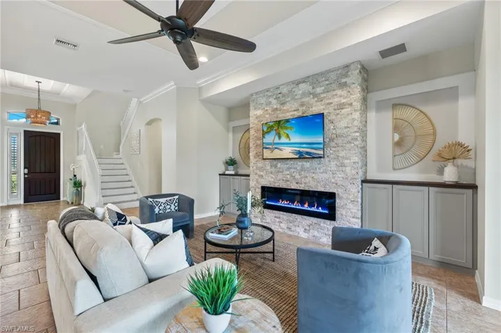 Living room with ceiling fan, crown molding, and a stone fireplace