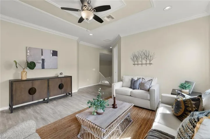 Living room with ornamental molding, wood-type flooring, a tray ceiling, and ceiling fan