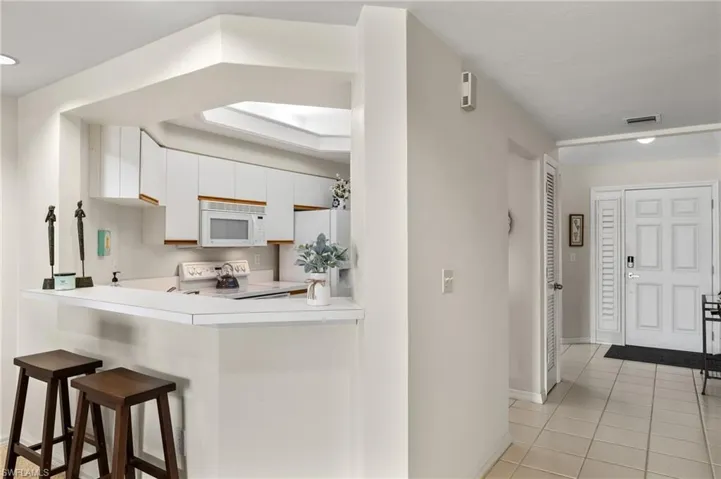 Kitchen with a kitchen breakfast bar, white appliances, white cabinetry, and light tile floors