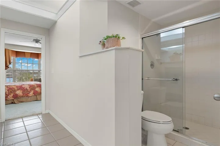 Bathroom with an enclosed shower, tile flooring, ceiling fan, and toilet
