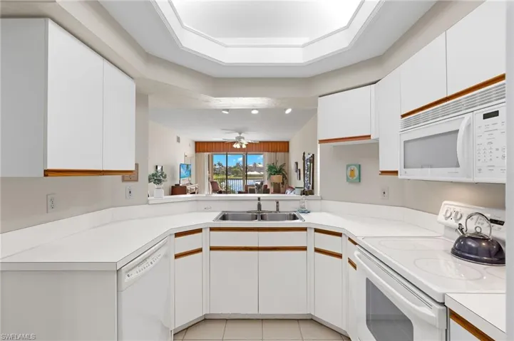 Kitchen featuring ceiling fan, white appliances, light tile flooring, sink, and white cabinets