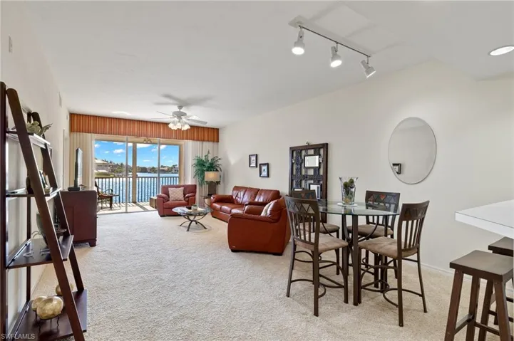 Living room with light colored carpet, track lighting, a water view, and ceiling fan