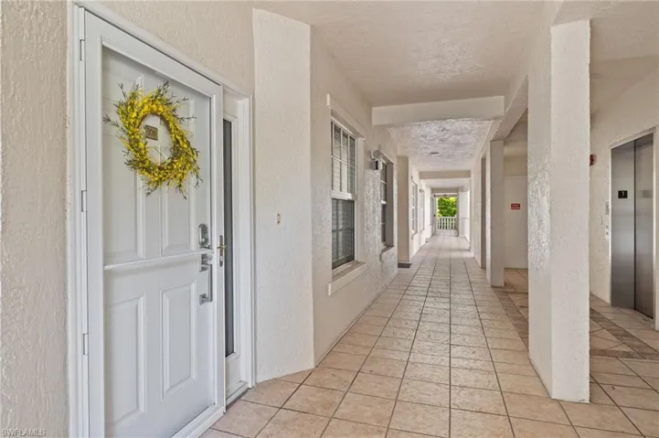 Corridor with a textured ceiling, light tile flooring, and elevator