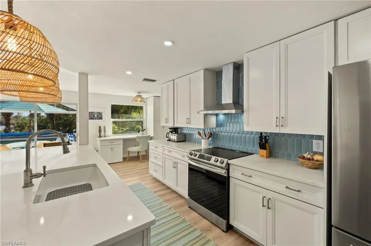 Kitchen featuring stainless steel appliances, wall chimney range hood, white cabinetry, light stone counters, and backsplash