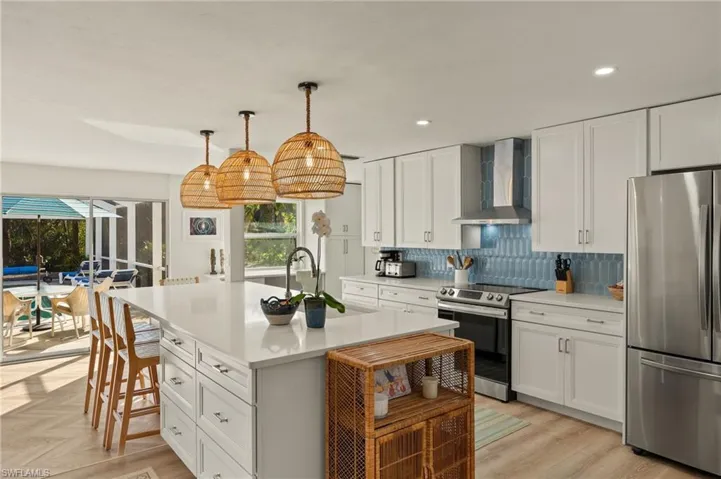 Kitchen with appliances with stainless steel finishes, white cabinets, wall chimney range hood, a kitchen bar, and backsplash