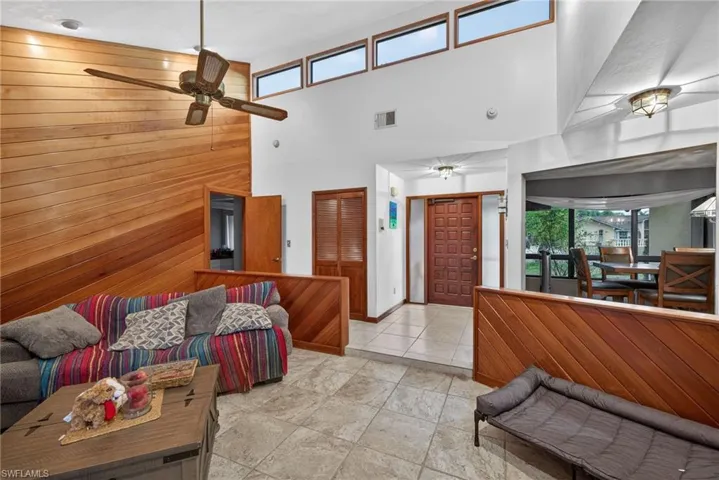 Living room featuring wood walls, a high ceiling, and ceiling fan