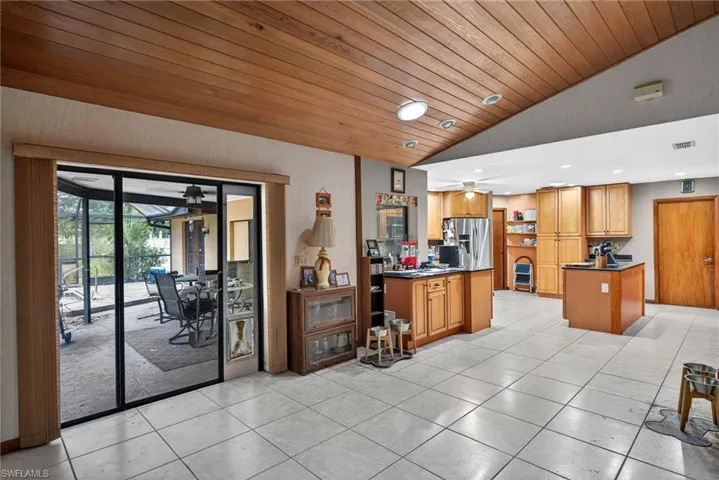 Kitchen with dark countertops, a ceiling fan, wood finish cabinetry, a sunroom, and stainless steel fridge with ice dispenser