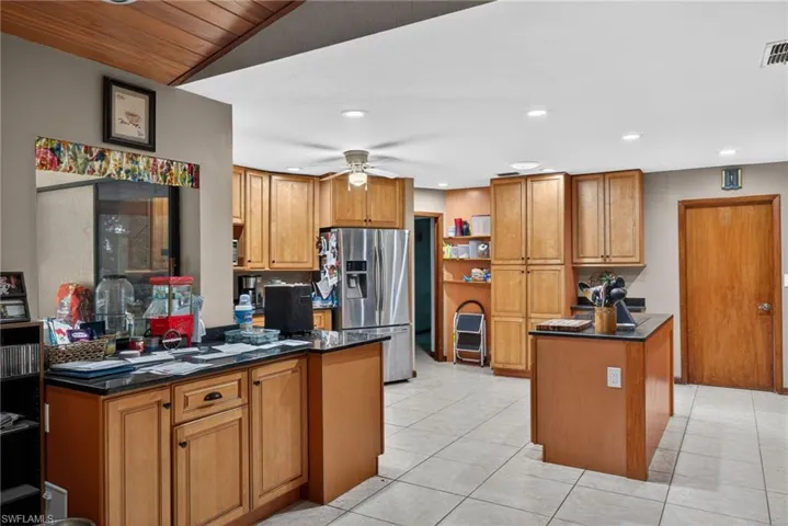 Kitchen featuring wood finish cabinets, stainless steel refrigerator with ice dispenser, a ceiling fan, light tile patterned floors, and dark stone countertops