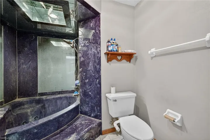 Full bath with a combined bath / shower with marble appearance and toilet