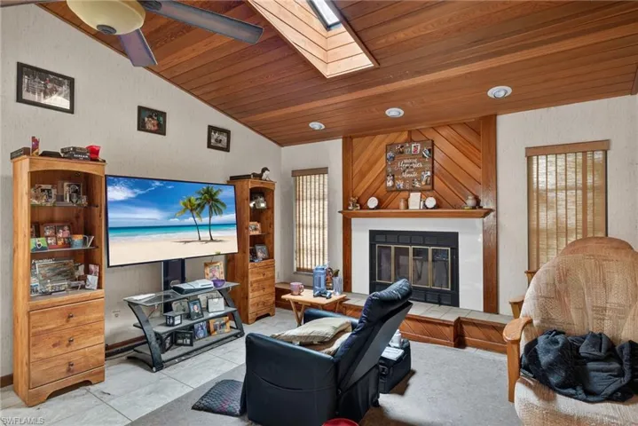 Living room with a tiled fireplace, a skylight, ceiling fan, tile patterned flooring, and a vaulted wood ceiling
