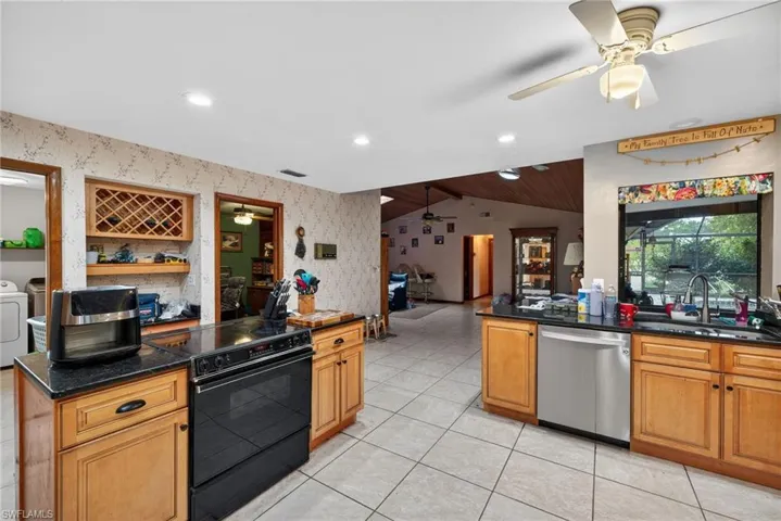 Kitchen with black range with electric stovetop, vaulted ceiling, dishwasher, dark stone countertops, and wood finish cabinetry