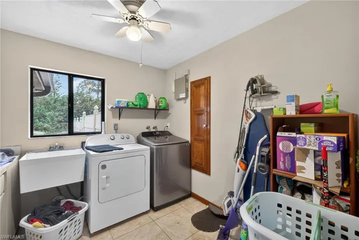 Laundry room with washing machine and dryer, ceiling fan, light tile patterned floors, and electric panel