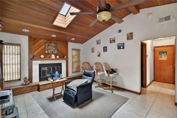 Living area featuring a glass covered fireplace, a ceiling fan, a skylight, a high wood beamed ceiling, and light tile patterned floors