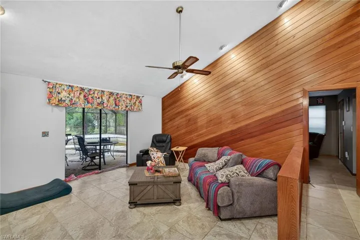 Living area featuring wood walls, lofted ceiling, ceiling fan, and tile patterned floors