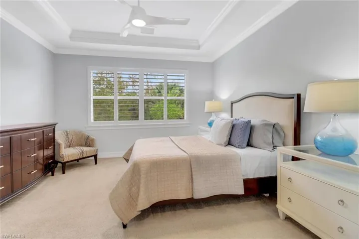Bedroom featuring light carpet, ornamental molding, a raised ceiling, and ceiling fan
