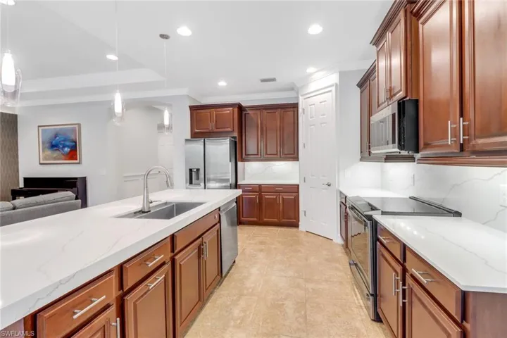 Kitchen featuring appliances with stainless steel finishes, sink, hanging light fixtures, light stone counters, and decorative backsplash