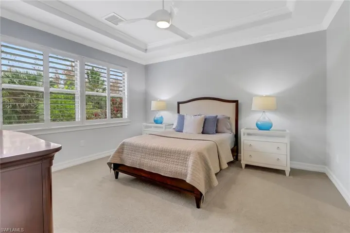Bedroom with light carpet, ornamental molding, a tray ceiling, and ceiling fan