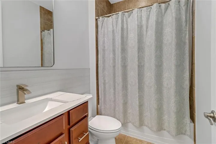 Full bathroom featuring shower / bath combination with curtain, toilet, tile patterned floors, tile walls, and vanity