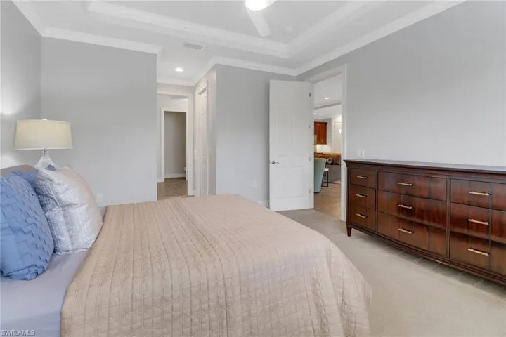Bedroom with crown molding, a raised ceiling, light carpet, and ceiling fan
