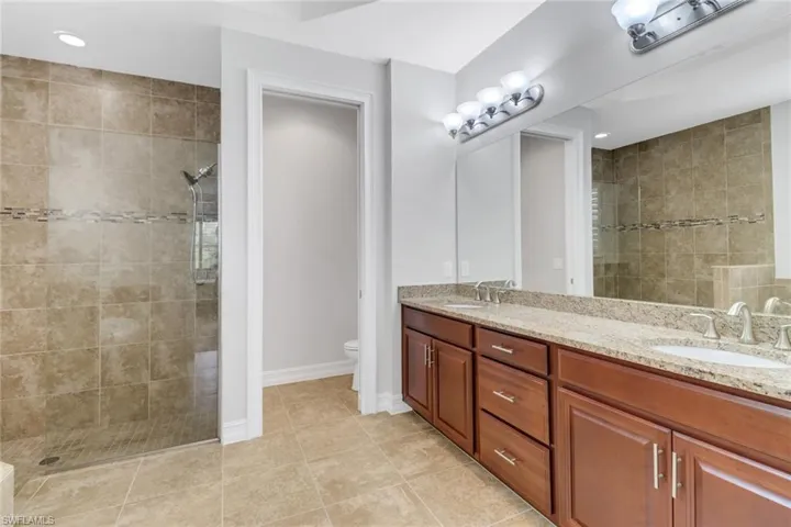 Bathroom featuring vanity, tiled shower, toilet, and tile patterned flooring