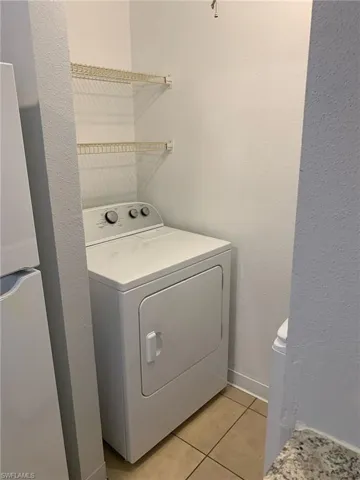 Laundry area featuring washer / clothes dryer, a textured wall, and light tile patterned floors
