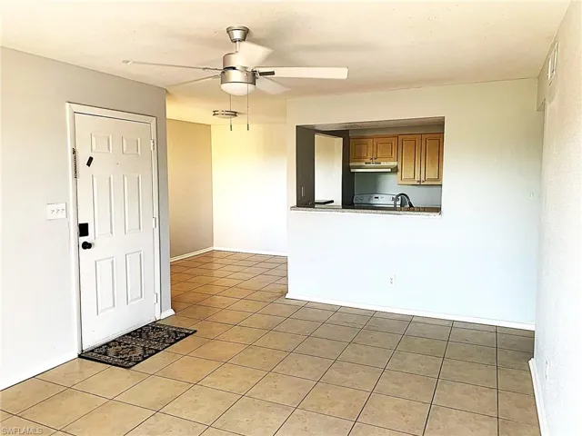 Kitchen featuring ceiling fan, brown cabinets, under cabinet range hood, light tile patterned floors, and stove