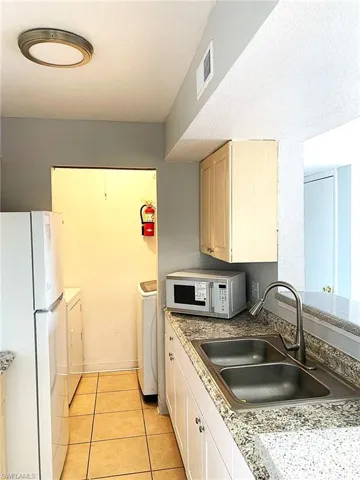 Kitchen featuring separate washer and dryer, white appliances, light brown cabinetry, light tile patterned floors, and light countertops