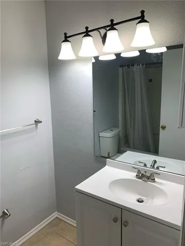 Full bath featuring a shower with shower curtain, a textured wall, vanity, and light tile patterned floors